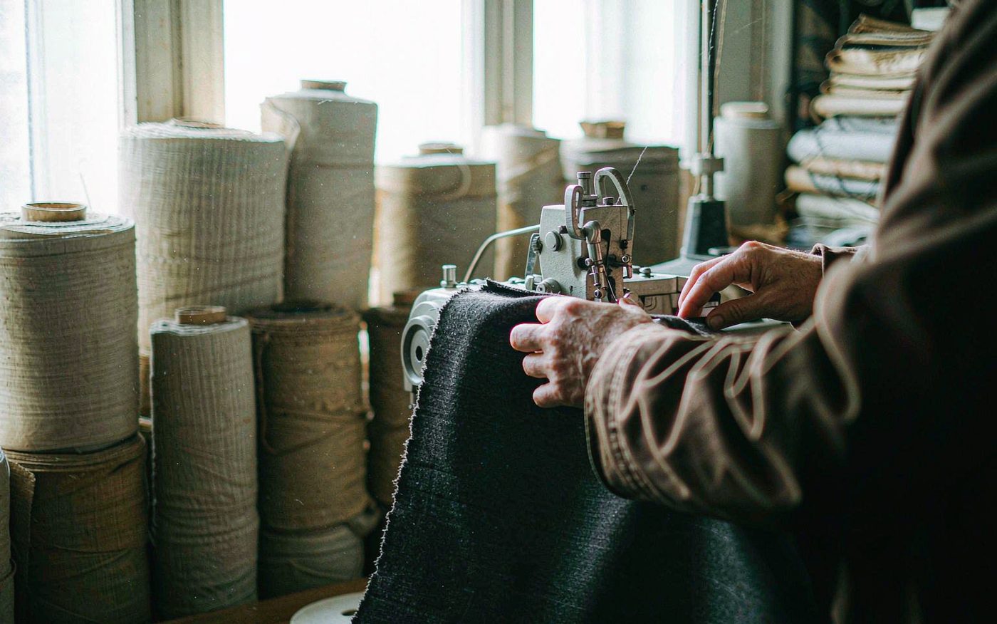 Hands guiding fabric through an industrial sewing machine in the atelier