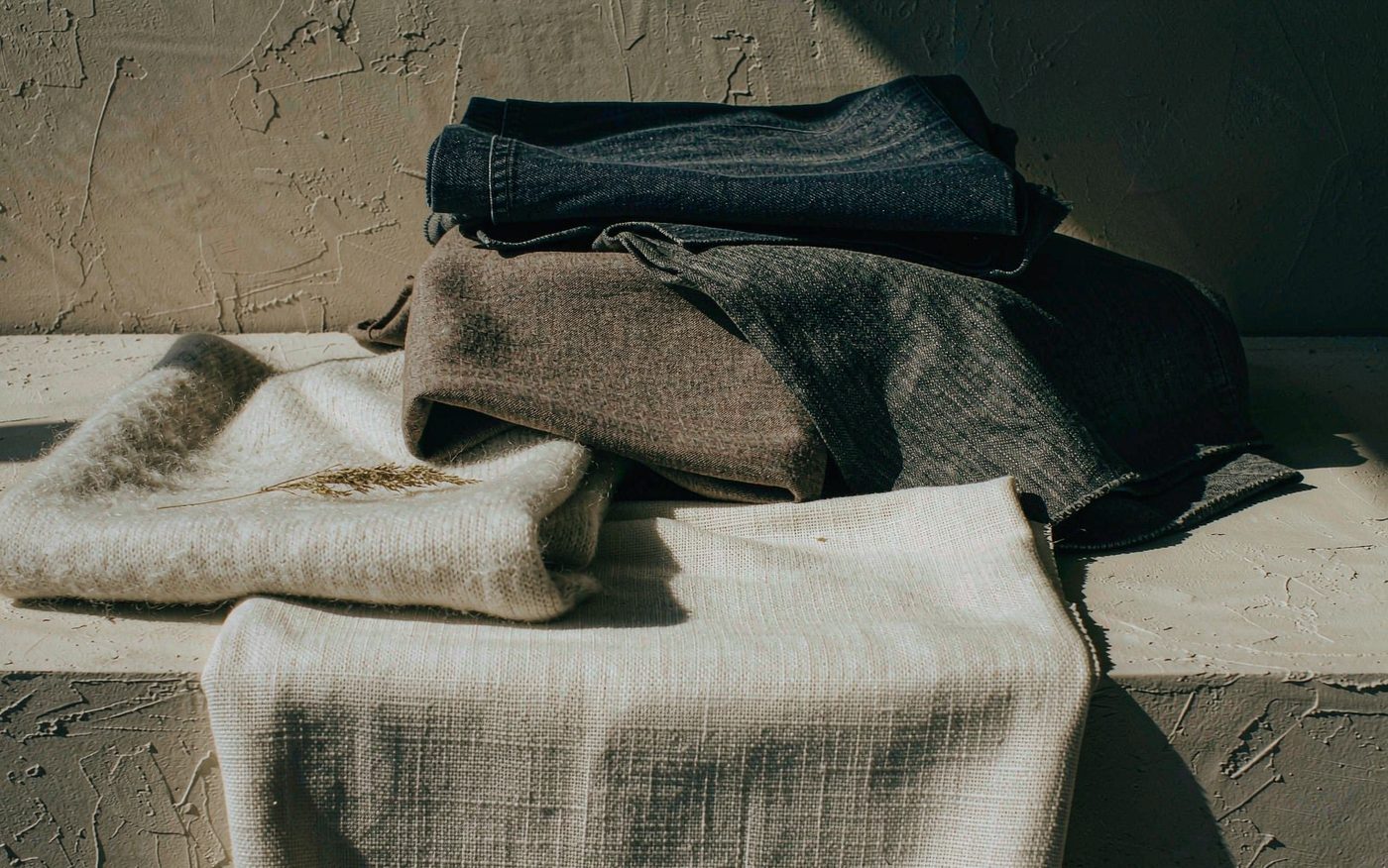 Folded natural fabric swatches — organic cotton, lambswool, wool suiting and denim